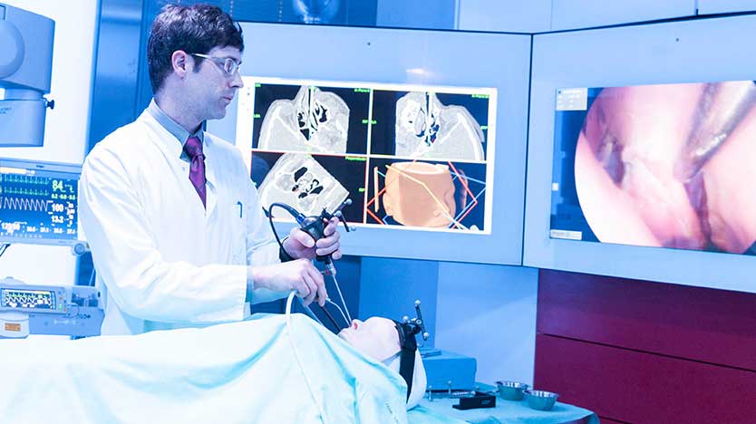 Dr. Mathias Hofer führt ein Endoskop und ein chirurgisches Instrument in das rechte Nasenloch eines Dummy-Patienten ein.