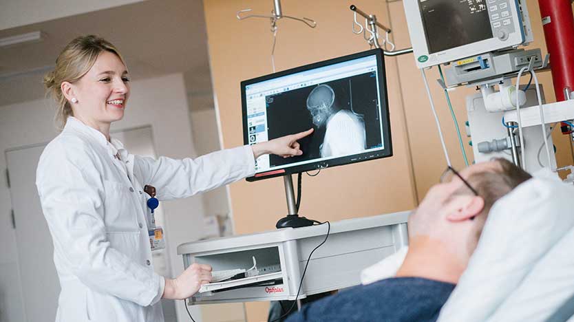 Ärztin zeigt liegendem Patienten Röntgenaufnahme; Quelle: BMWi / Ole Spata