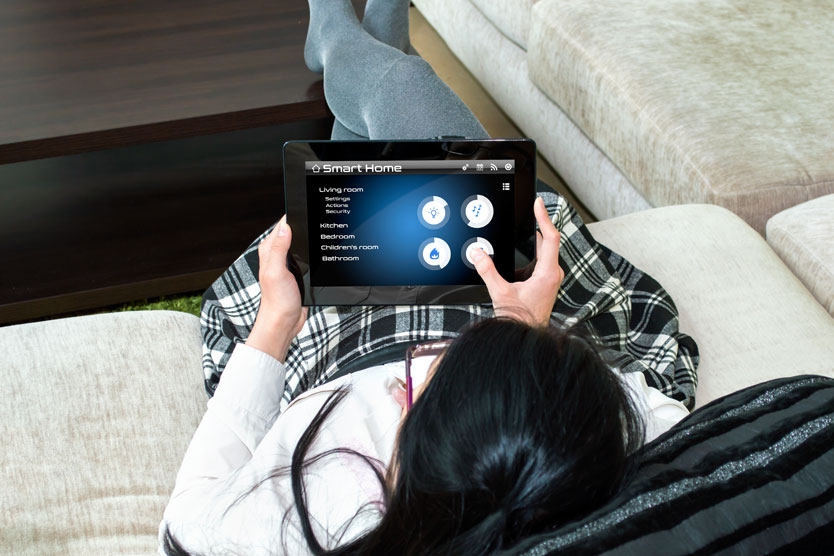 Frau sitzt vor Tablet, mit dem sie Smart Home steuert