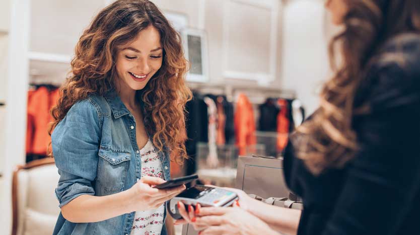 Junge Frau bezahlt im Modekaufhaus mit dem Smartphone