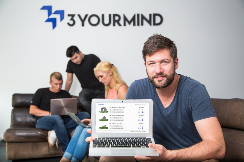 Dieses Bild zeigt Stephan Kühr, Gründer und CEO des Start-ups 3Yourmind, wie er einen Computer in die Kamera hält. Im Hintergrund sind das Firmenlogo an einer Wand zu sehen, davor sitzen 3 Menschen auf einem Sofa und arbeiten.
